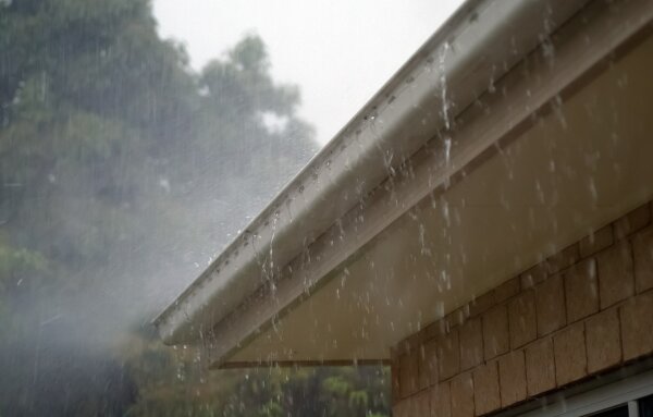 Na zdjęciu kawalek rynny przy dachowej z której ścieka deszcz