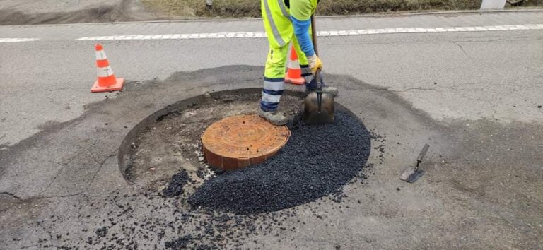 na zdjęciu właz kanalizacyjny, który jest obudowany asfaltem obok pracownik ze sprzętem utwardzającym asfalt