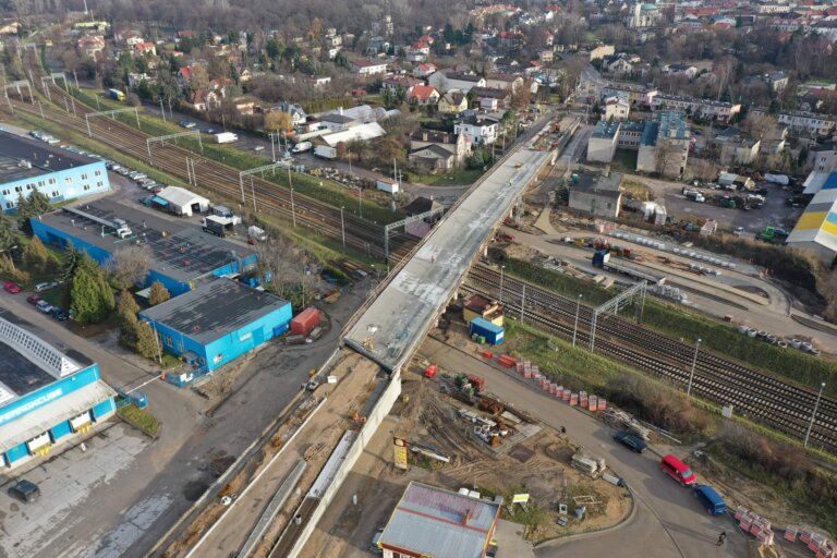 Na zdjęciu pokazana budowa Wiaduktu przy ul. Zwierzynieckiej w Skierniewicach. pod wiaduktem widoczne tory, obok z lotu ptaka fabryka, przejeżdżające auta oraz w tle domy mieszkańców