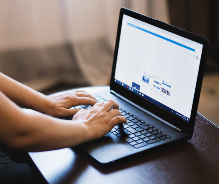 na zdjęciu otworzony czarny komputer - laptop w na nim ręce człowieka które są na klawiaturze