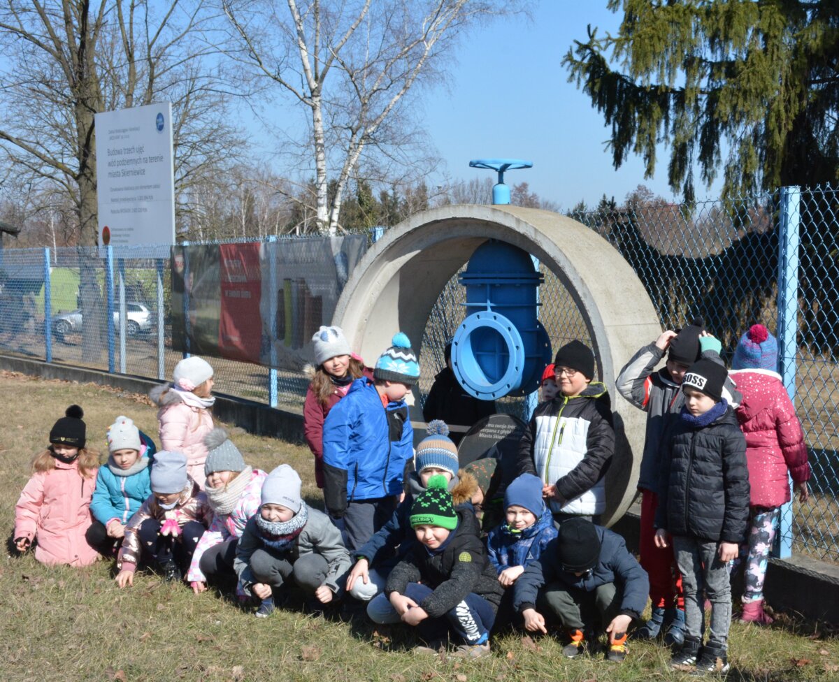 Na zdjęciu grupa dzieci pozujących przy rzeźbie betonowej okrągłej a na niej filtr do uzdatniania wody